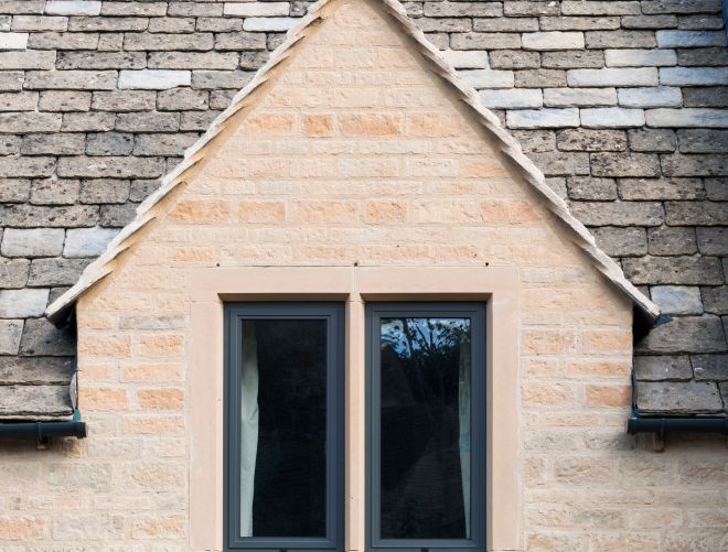 Two windows on the front of a house with roof tiles in view